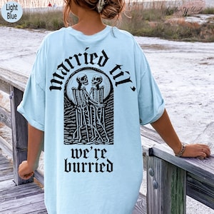 May include: Light blue t-shirt with a black graphic of two skeletons holding hands and the text "married til we're buried".