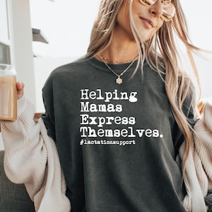 May include: Dark gray sweatshirt with the text "Helping Mamas Express Themselves." in white, along with the hashtag #lactationsupport. The sweatshirt is worn by a person with long blonde hair and sunglasses.