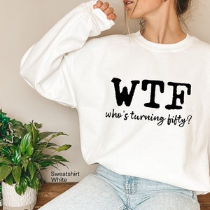 May include: White sweatshirt with black text that reads "WTF who's turning fifty?"