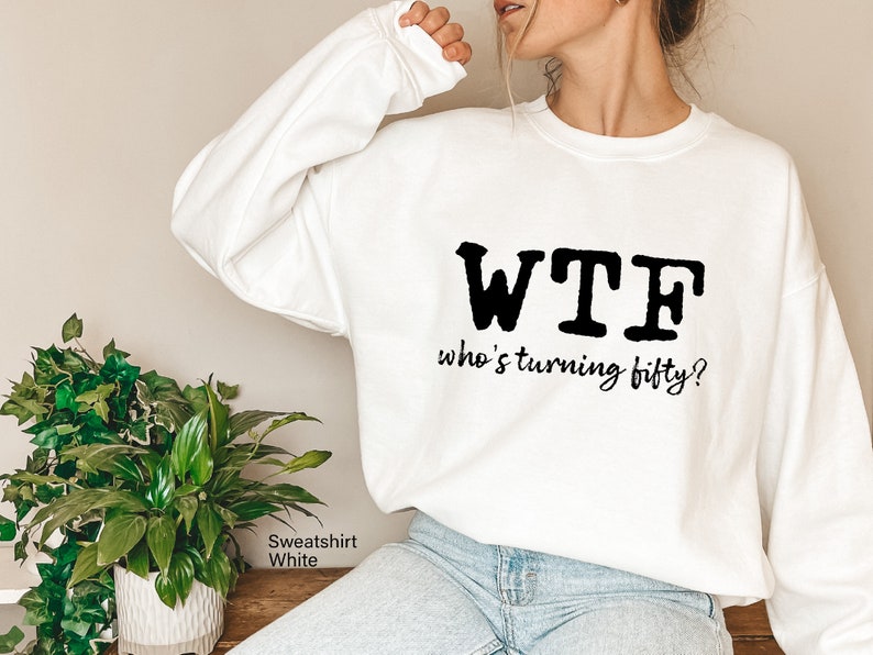 May include: White sweatshirt with black text that reads "WTF who's turning fifty?"
