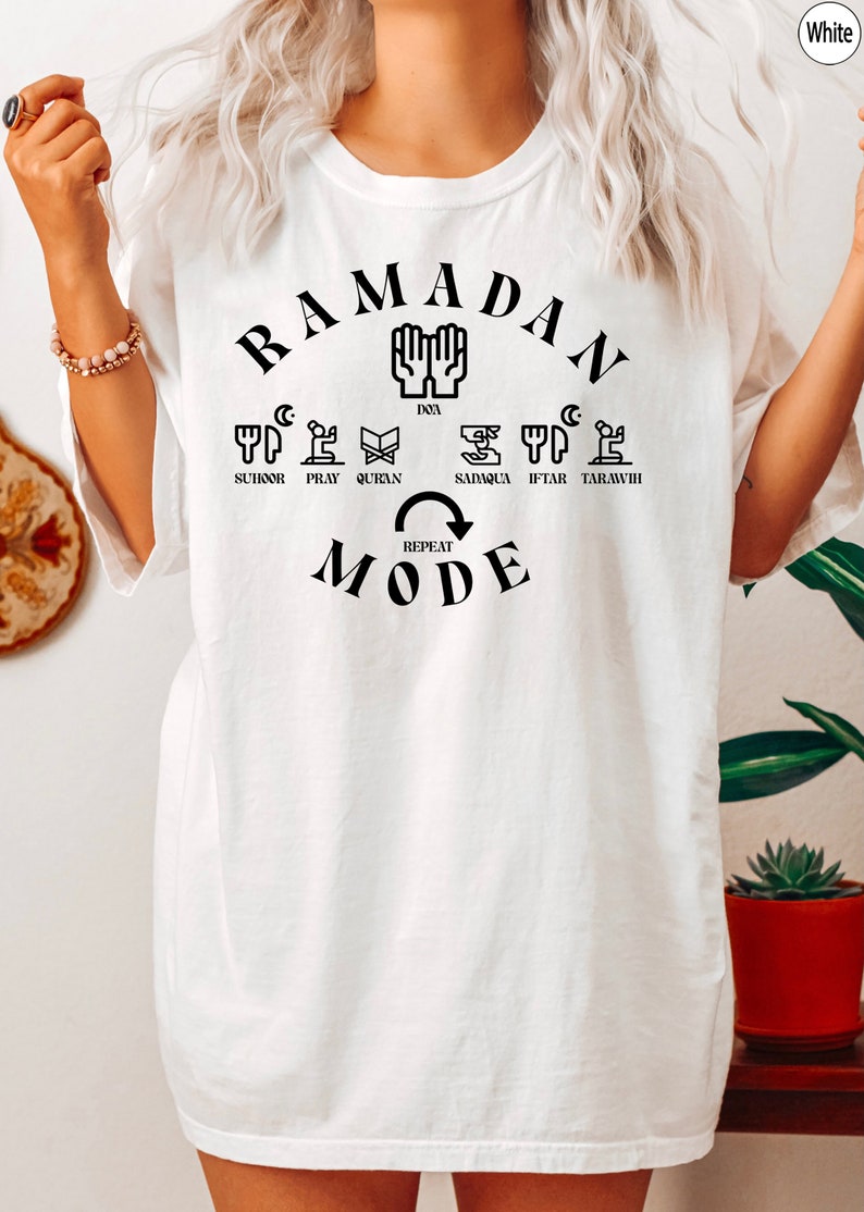 Pu&ograve; includere: Maglietta bianca con testo nero che recita "Ramadan Mode" e include un cerchio di icone che rappresentano diversi aspetti del Ramadan, tra cui suhur, preghiera, Corano, sadaqa, iftar e taraweeh.