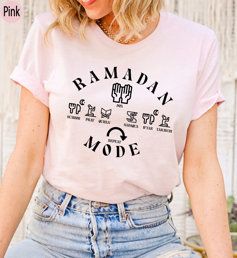 Pu&ograve; includere: Maglietta rosa con il testo "RAMADAN MODE" in nero. Il testo &egrave; circondato da un cerchio di icone che rappresentano le pratiche quotidiane del Ramadan, tra cui suhur, preghiera, Corano, sadaqa, iftar e tarawih.