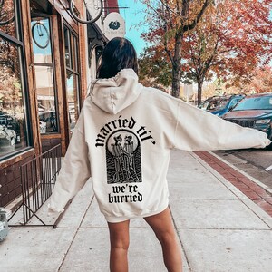 May include: A cream-colored hoodie with a black graphic print of two skeletons holding hands and the text "married til we're buried".