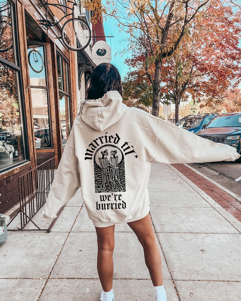 May include: A cream-colored hoodie with a black graphic print of two skeletons holding hands and the text "married til we're buried".
