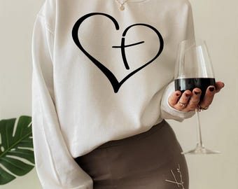 May include: A white long-sleeve sweatshirt featuring a black graphic of a heart with a cross integrated into the center. The sweatshirt has a crew neckline and ribbed cuffs, providing a clean and simple look for casual wear in any season.