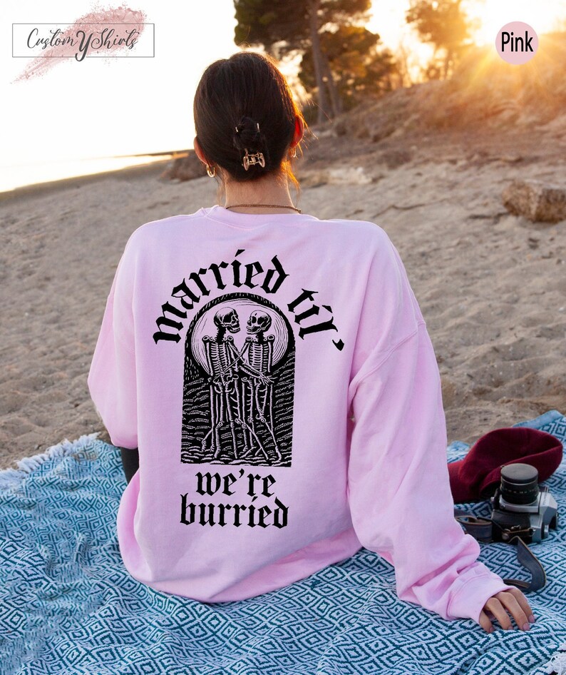 May include: A pink sweatshirt with a black graphic of two skeletons holding hands and the text "married til we're buried".