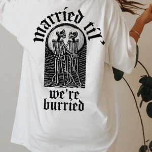 May include: White oversized t-shirt with a black graphic of two skeletons dancing with the text "married til we're buried" printed on the back.