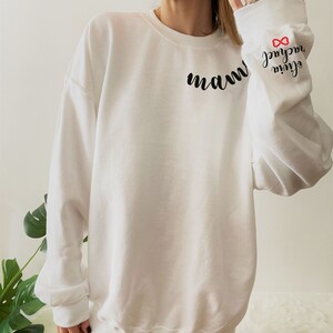 Może przedstawiać: Biała bluza z nadrukiem słowa "mam" z przodu i napisami "my girl" oraz symbolem nieskończoności na rękawie. Symbol nieskończoności jest czerwony.