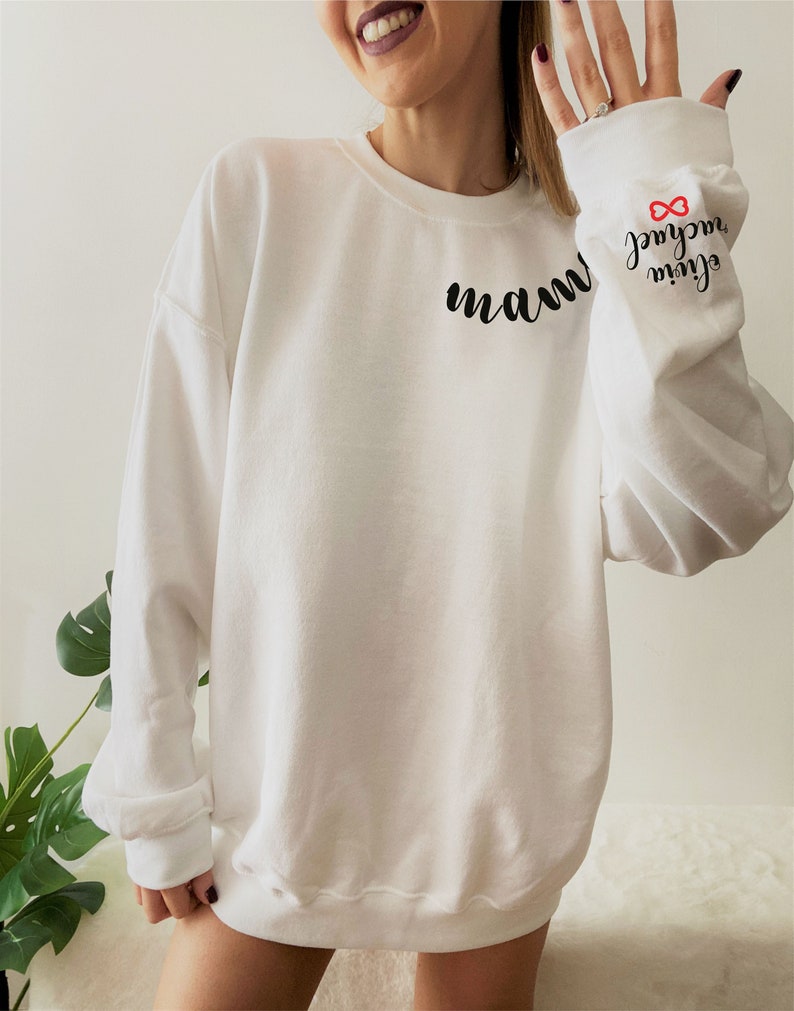 Może przedstawiać: Biała bluza z nadrukiem słowa "mam" z przodu i napisami "my girl" oraz symbolem nieskończoności na rękawie. Symbol nieskończoności jest czerwony.