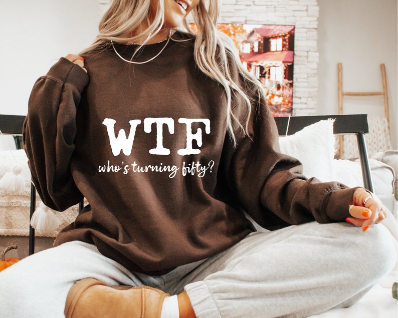 May include: A brown sweatshirt with the text "WTF who's turning fifty?" printed in white.