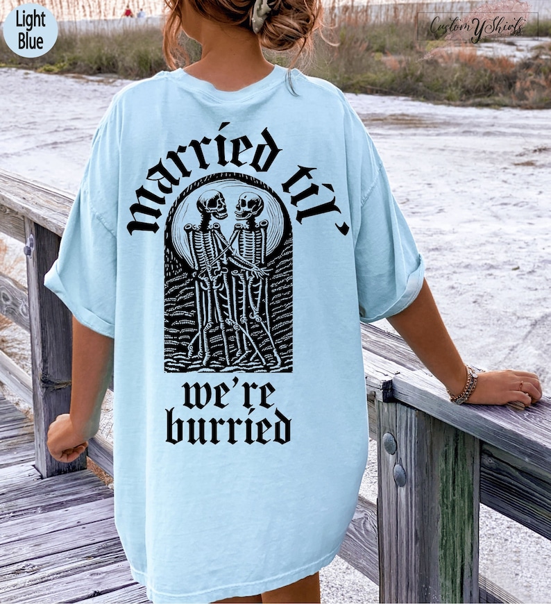 May include: Light blue t-shirt with a black graphic of two skeletons holding hands and the text "married til we're buried".