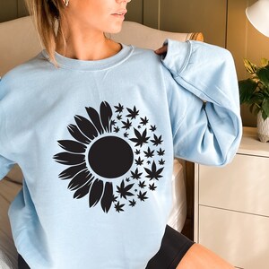 May include: A light blue sweatshirt with a black sunflower design. The sunflower is made up of marijuana leaves.