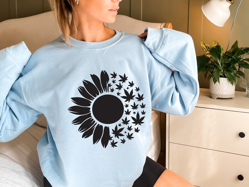May include: A light blue sweatshirt with a black sunflower design. The sunflower is made up of marijuana leaves.