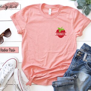A heather peach short-sleeve t-shirt featuring a small graphic on the left chest of a red strawberry with green leaves and the word CUSTOM printed in white across the center of the fruit