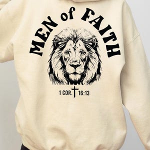 May include: A cream colored hoodie with a black lion graphic and the text "Men of Faith" and "1 Cor. 16:13".