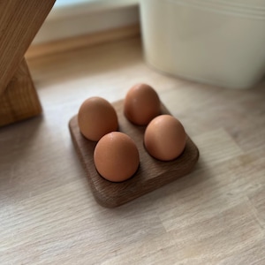 May include: A wooden egg holder with four brown eggs inside. The holder is made of dark wood and has a square shape.