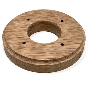 Op de afbeelding: Een ronde houten basis met een gat in het midden en vijf gelijkmatig verdeelde gaten rond de rand. De basis is gemaakt van lichtbruin hout en heeft een gladde afwerking.