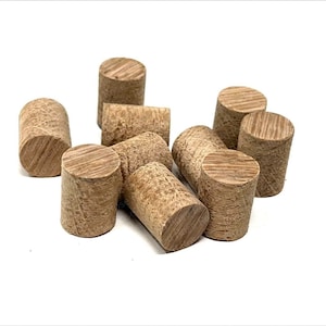 Puede incluir: Un conjunto de pequeñas espigas de madera cilíndricas, de color marrón claro y con veta visible. Las espigas están cortadas con una parte superior e inferior planas, sobre un fondo blanco.
