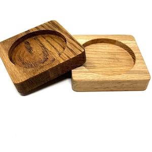 Puede incluir: Dos posavasos de madera con una hendidura circular en el centro. Los posavasos están hechos de madera marrón claro con un patrón de veta natural.