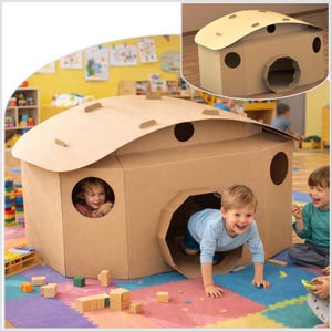 Könnte beinhalten: Ein großes Spielhaus aus braunem Karton mit geschwungenem Dach und runden Fenstern. Kinder spielen in und um die Struktur herum. Das Spielhaus hat einen tunnelartigen Eingang und ist von bunten Spielmatten und Holzblöcken umgeben.