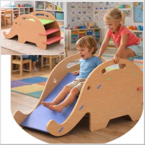 Puede incluir: Una estructura de escalada de madera con forma de elefante con tobogán y escalones. El tobogán es azul y los escalones son rosas y verdes. Un niño pequeño se desliza por el tobogán, con la ayuda de otro niño. Para jugar en interiores.