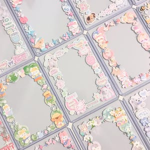 May include: A collection of rectangular plastic card holders decorated with various colorful stickers featuring cartoon animals, flowers, stars, and Korean text. Each clear frame is bordered by a unique arrangement of adhesive decals in pastel tones.