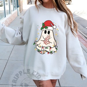 May include: A white sweatshirt with a cartoon ghost wearing a Santa hat and holding a candy cane. The ghost is surrounded by Christmas lights. The sweatshirt is a light gray color and has a relaxed fit.