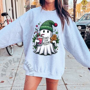May include: A gray sweatshirt with a cartoon ghost wearing a Santa hat and holding a gingerbread man. The ghost is holding a glass of red liquid and has the text "Don't Stop Believin'" on it.