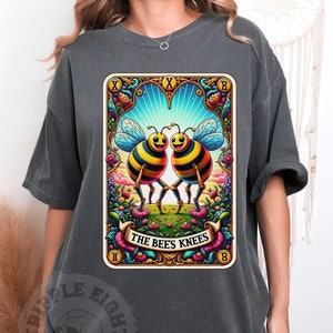 May include: A dark gray t-shirt with a vintage-style illustration of two bees with the text "The Bees Knees" on a card.
