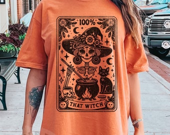 May include: Orange t-shirt with a black and white illustration of a skeleton witch with a cauldron, a black cat, and the text "100% That Witch".