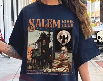 May include: Black t-shirt with a graphic featuring the text "SALEM BOOK CLUB" and illustrations of a haunted house, a full moon with bats, and a skull atop books. The shirt also includes the text "JOIN OUR COVEN OF READERS FOR SPOOKY STORIES & SPELLS."