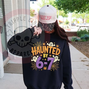 May include: Black sweatshirt with the text "HAUNTED BY 6-7" in orange and purple, featuring ghost and spiderweb graphics. A white baseball cap with "I LOVE YOU" text is also visible.