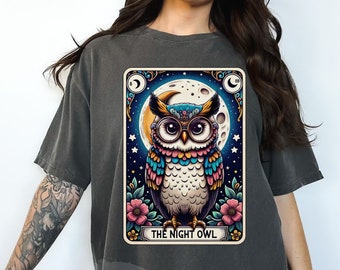 May include: A dark gray t-shirt with a vintage-style tarot card design featuring an owl with colorful feathers and the text "The Night Owl".