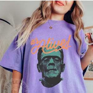 May include: Purple t-shirt with a graphic of Frankenstein's monster and the text "It's Alive!" in orange.