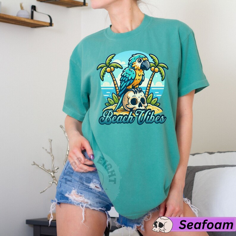 May include: A teal blue t-shirt with a cartoon parrot sitting on a skull with palm trees in the background. The text "Beach Vibes" is printed on the shirt.