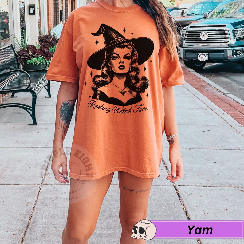 May include: A woman wearing an orange t-shirt with a black and white illustration of a witch with the text "Resting Witch Face".
