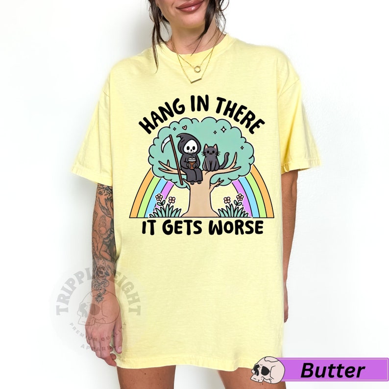 May include: Yellow t-shirt with a graphic of a grim reaper and a black cat sitting in a tree with a rainbow behind them. The text on the shirt reads "Hang in there it gets worse".