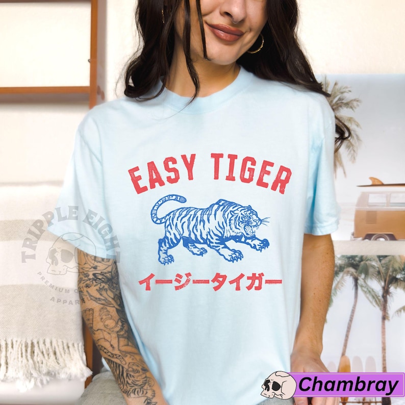May include: Pale blue t-shirt featuring the red text "EASY TIGER" above a blue and white tiger design. Japanese text is below the tiger. A casual wear item.