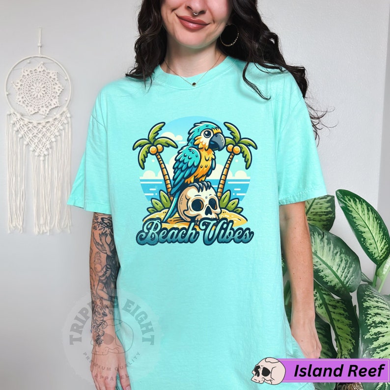 May include: A turquoise blue t-shirt with a cartoon parrot sitting on a skull with palm trees and the text "Beach Vibes".