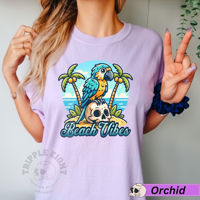 May include: A purple t-shirt with a cartoon parrot perched on a skull with palm trees and the text "Beach Vibes". The shirt has a logo on the bottom left corner that says "Triple Eight Premium Quality Apparel".