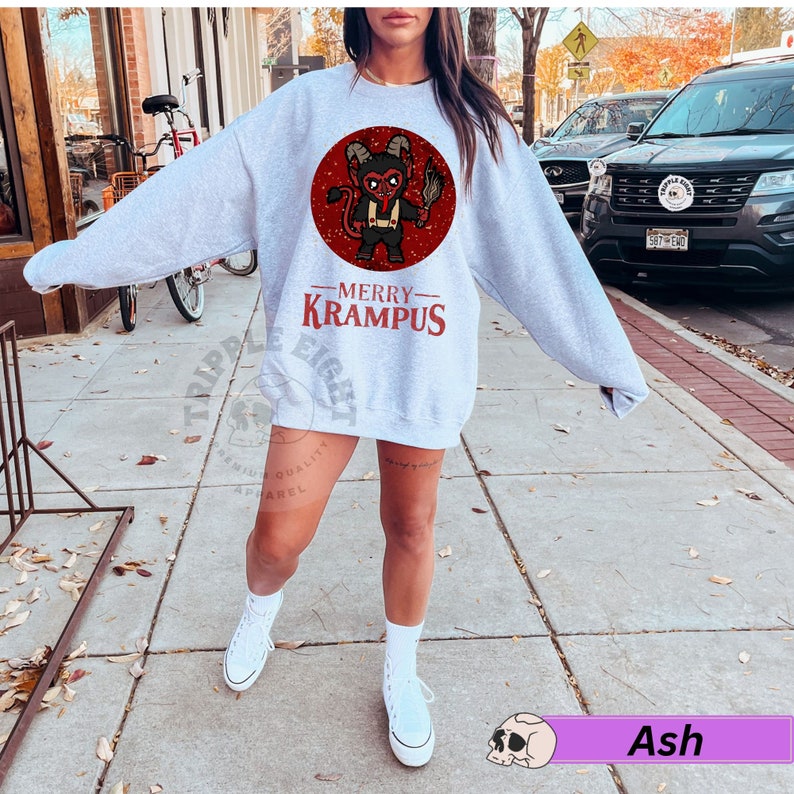 May include: A gray sweatshirt with a red circle graphic of a cartoon devil holding a torch. The text "Merry Krampus" is printed below the graphic.