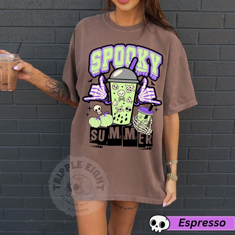 Puede incluir: Camiseta marr&oacute;n con un dise&ntilde;o gr&aacute;fico con las palabras "Spooky Summer" en verde y morado. El dise&ntilde;o incluye una bebida de dibujos animados con calaveras, manos de esqueleto y calabazas. La camiseta tambi&eacute;n tiene el texto "Triple Eight" y "Espresso".