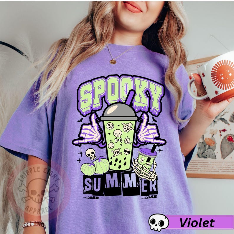 Puede incluir: Camiseta violeta con un dise&ntilde;o de verano espeluznante. El dise&ntilde;o presenta la palabra "Spooky" en verde, una mano de esqueleto, una bebida con calaveras y la palabra "Summer". La camiseta tambi&eacute;n tiene un peque&ntilde;o logotipo de calavera.