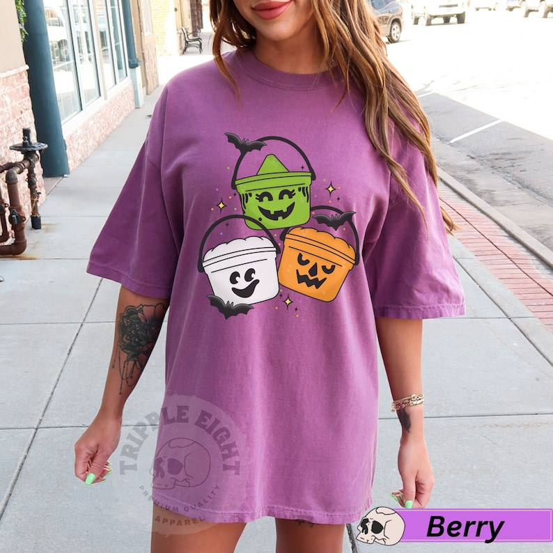 May include: Purple t-shirt featuring a graphic of three Halloween buckets with faces. The buckets are green, white and orange. The text "Triple Eight" is on the bottom left of the shirt.