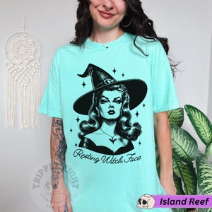 May include: A turquoise blue t-shirt with a black and white illustration of a witch with the text "Resting Witch Face".