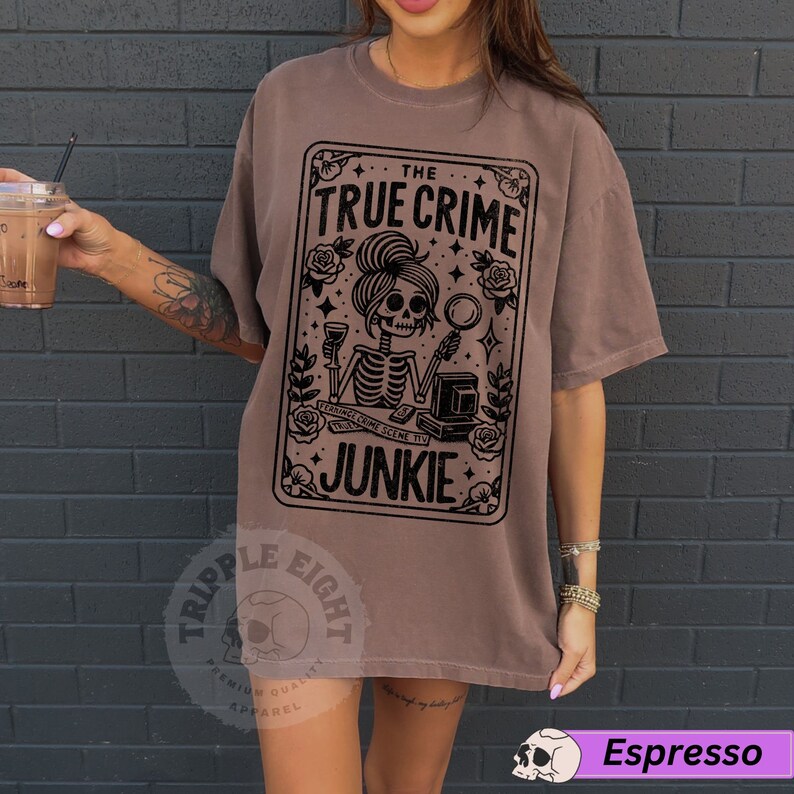 Puede incluir: Una camiseta marr&oacute;n con un dise&ntilde;o gr&aacute;fico negro de un esqueleto sosteniendo una copa de vino y una lupa. El gr&aacute;fico est&aacute; rodeado de rosas y el texto "The True Crime Junkie".