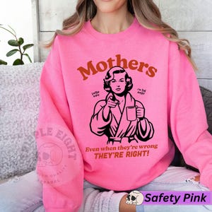Op de afbeelding: Roze sweatshirt met een afbeelding van een vrouw in een badjas die een kop koffie vasthoudt. De tekst "Mothers" staat in oranje boven de afbeelding en de tekst "Even when they're wrong THEY'RE RIGHT!" staat onder de afbeelding.
