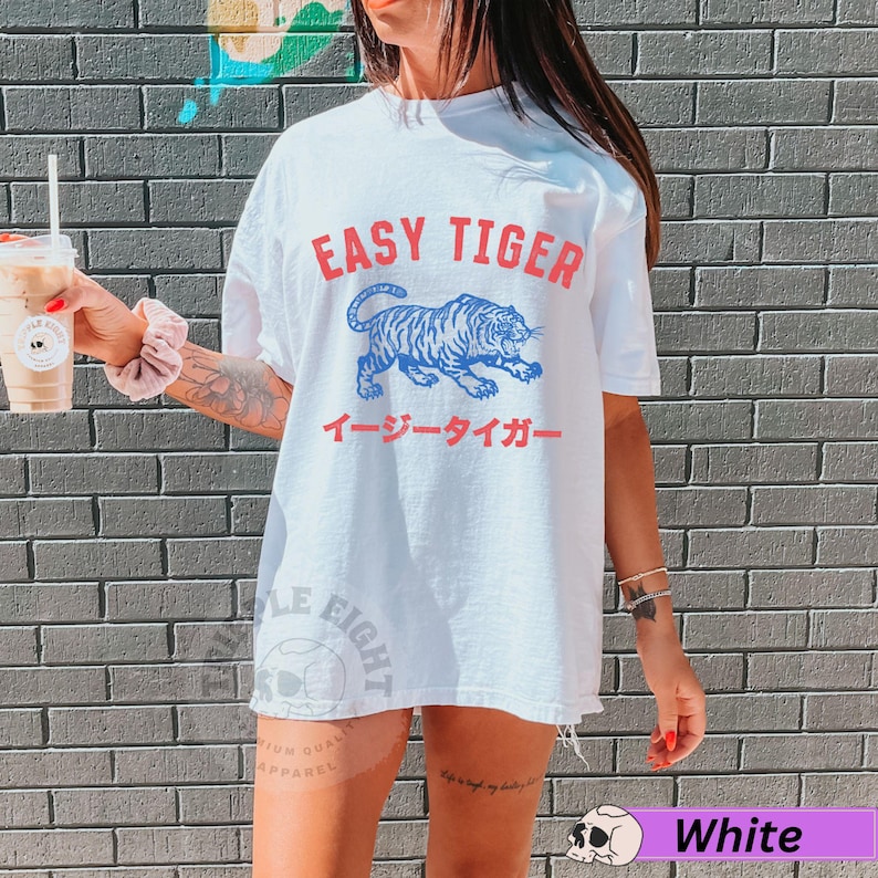 May include: White t-shirt featuring the text "EASY TIGER" in red, above a blue tiger illustration. Japanese text is below the graphic. The shirt has a relaxed, oversized fit.