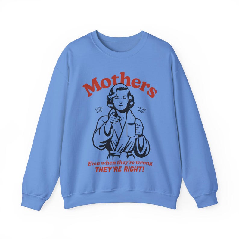 Op de afbeelding: Lichtblauwe trui met een rode afbeelding van een vrouw in een badjas die een mok vasthoudt. De tekst "Mothers" staat in het rood boven de vrouw en de tekst "Even when they're wrong THEY'RE RIGHT!" staat in het rood onder de vrouw.