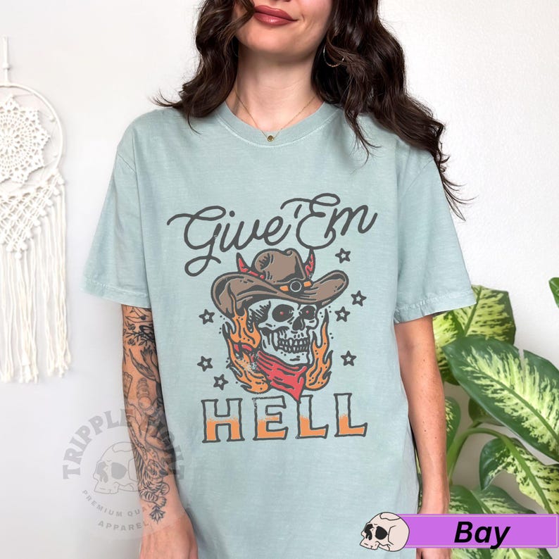 May include: A light blue t-shirt featuring a skull wearing a cowboy hat and the text "Give 'Em Hell".